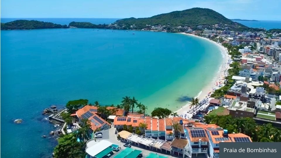 Praia de Bombinhas com águas cristalinas, visitantes nadando e praias conectadas ao fundo.