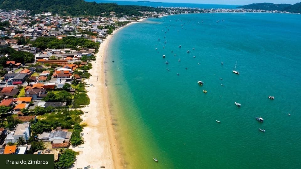 Praia de Zimbros com água calma, estrutura básica e vista do costão rochoso.