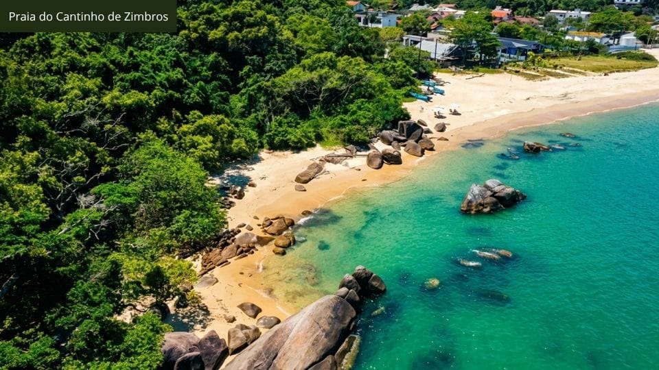 Praia pequena com fundo arenoso e costão rochoso, entrada da trilha Costeira dos Zimbros em Bombinhas.