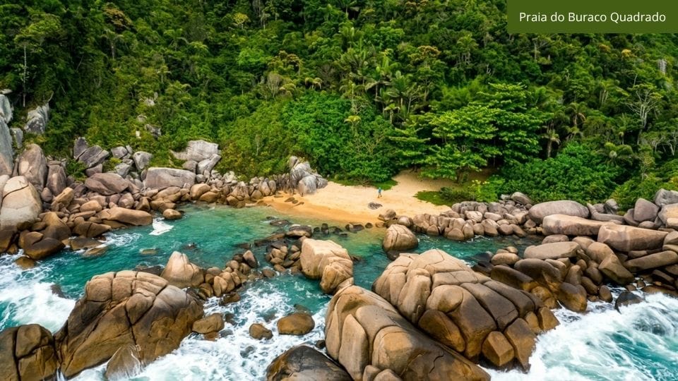 Praia do Buraco Quadrado com água cristalina, vegetação densa e formações rochosas.